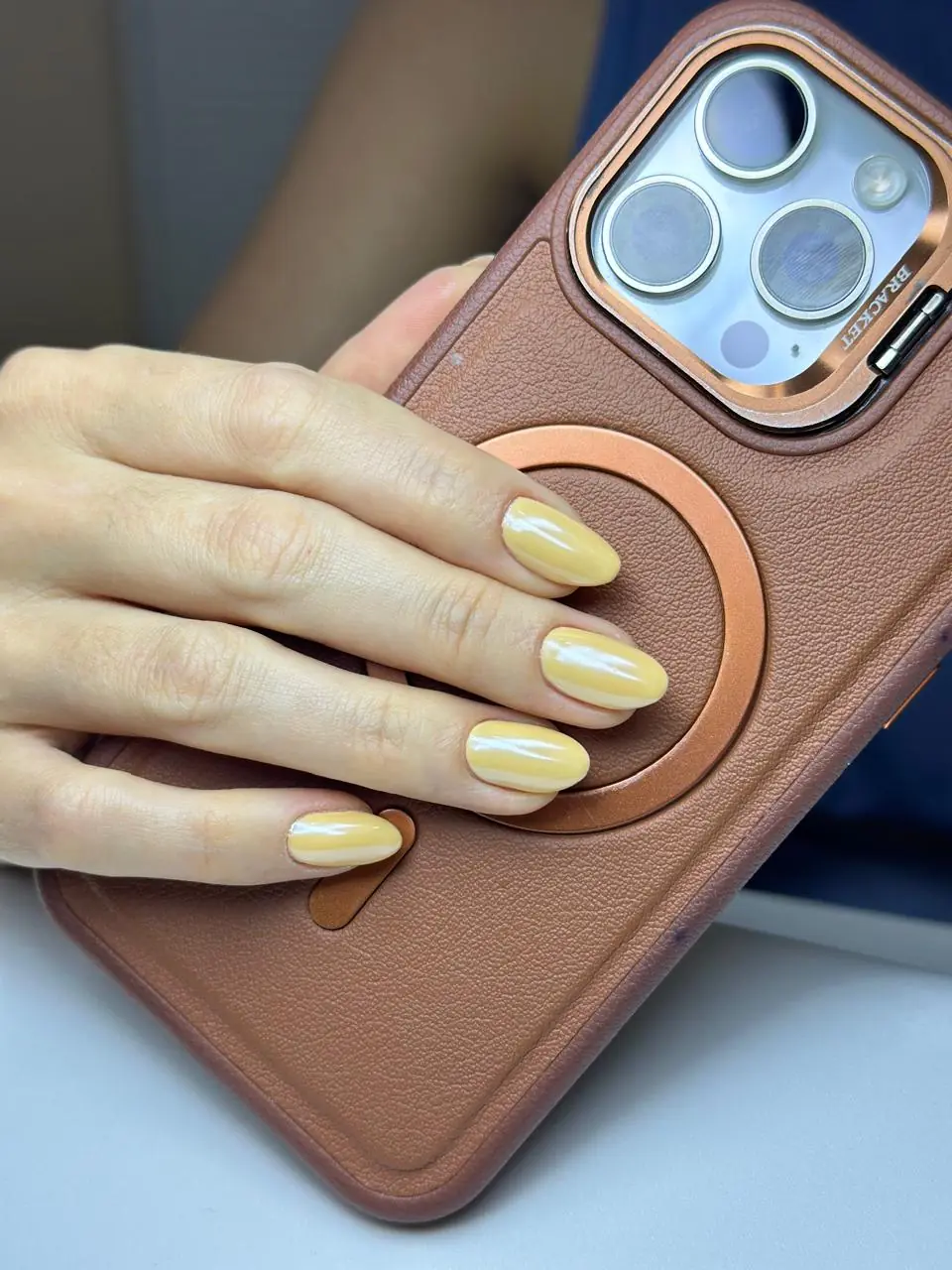Unhas amendoadas com esmaltação amarela sobre acessório caramelo